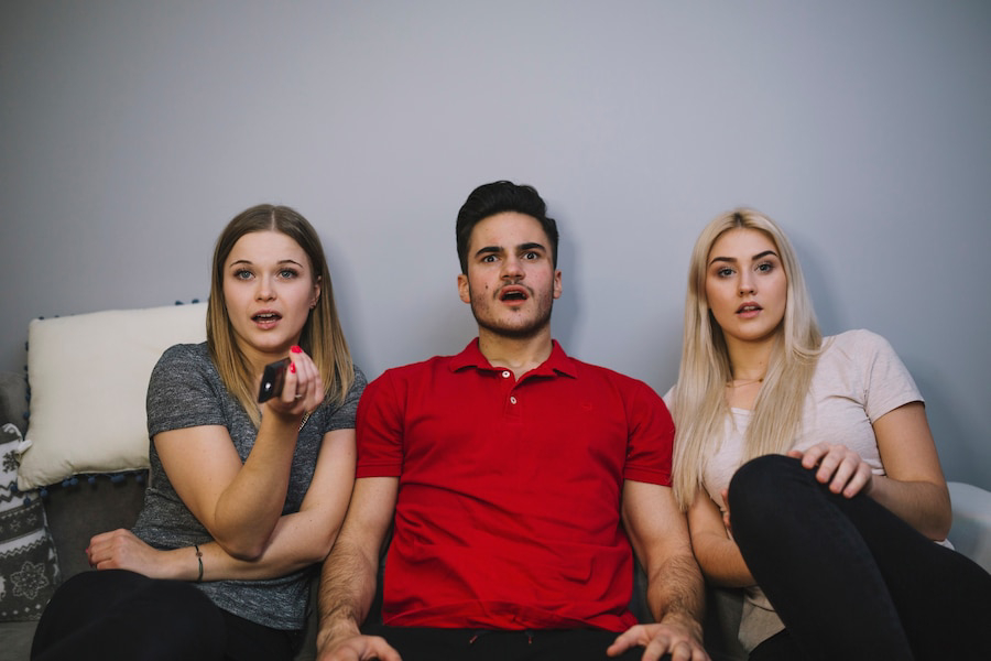 Three individuals sit closely together on a couch.