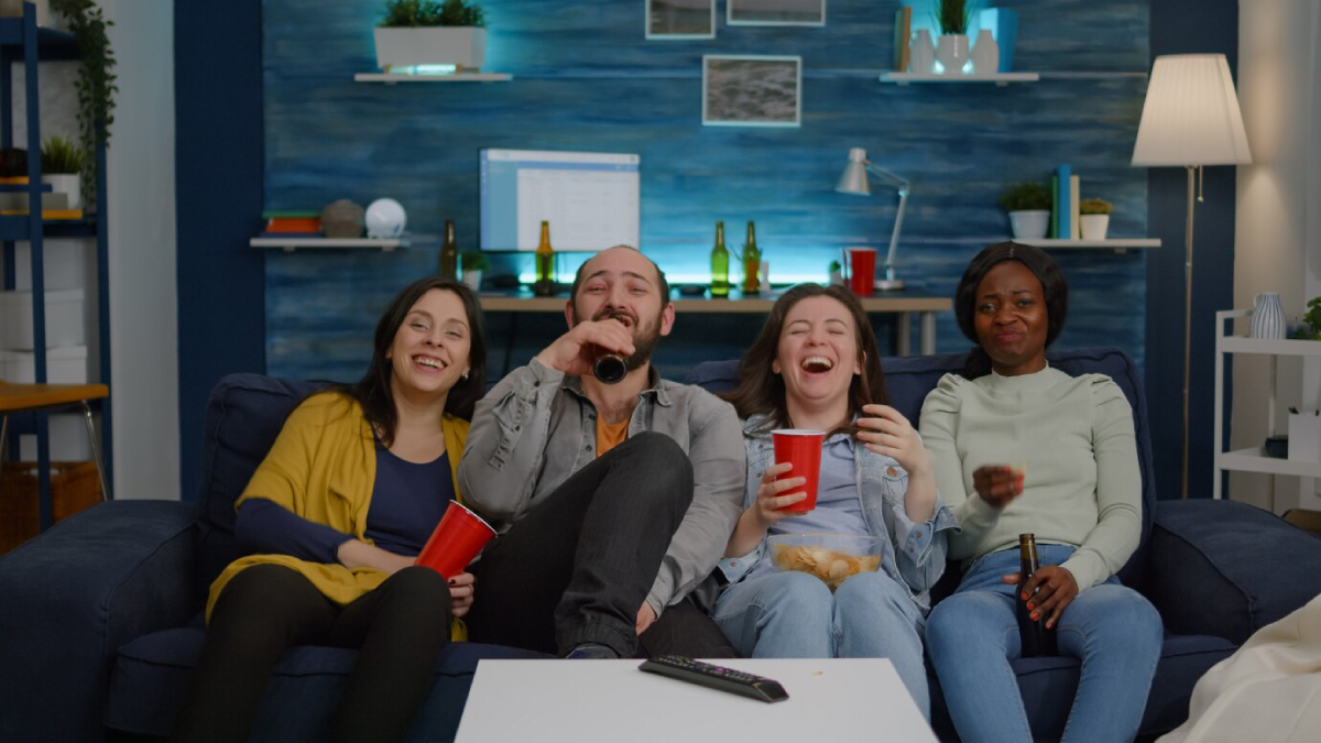 A group of friends sit on a couch, each holding drinks and snacks.