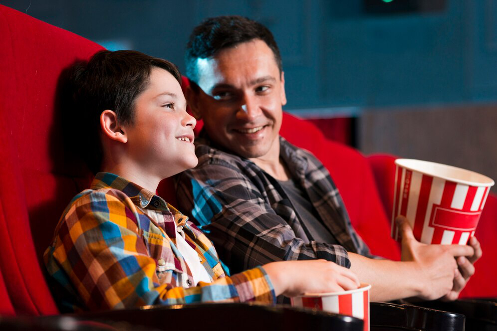 child and an adult sit closely together in a cinema.