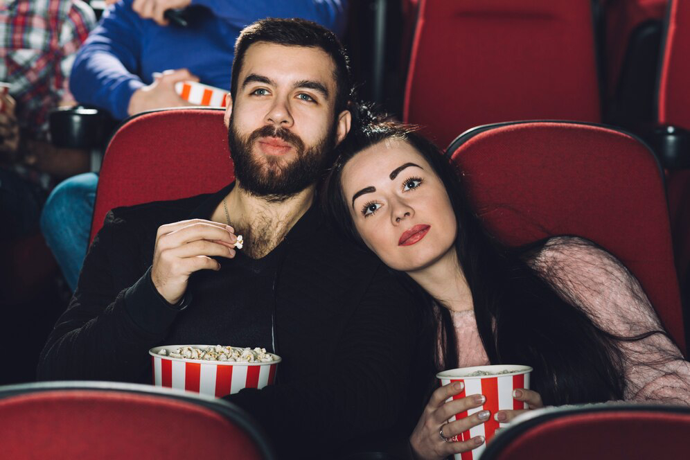 A couple enjoys popcorn together in a movie theater.
