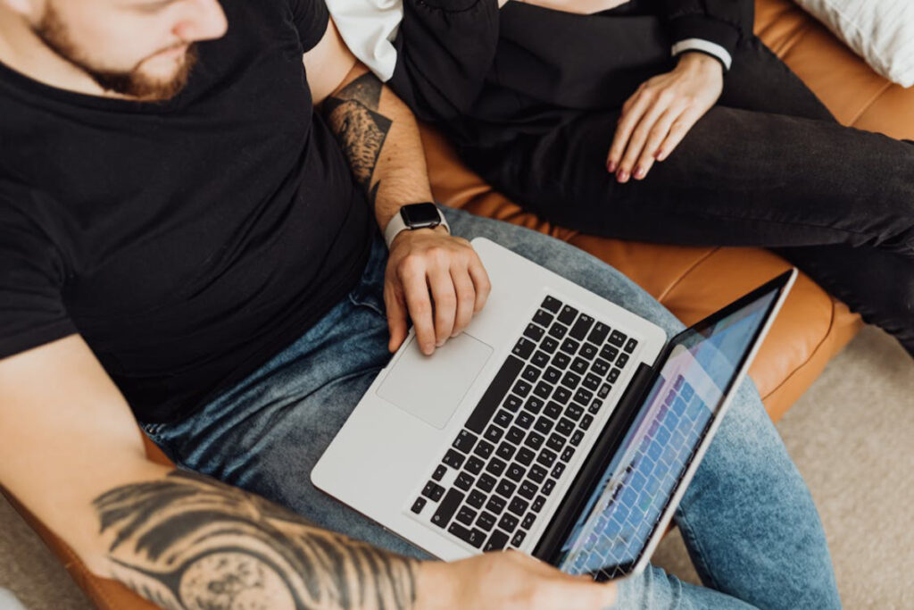 A close-up of a man with a beard and tattoo using a laptop.
