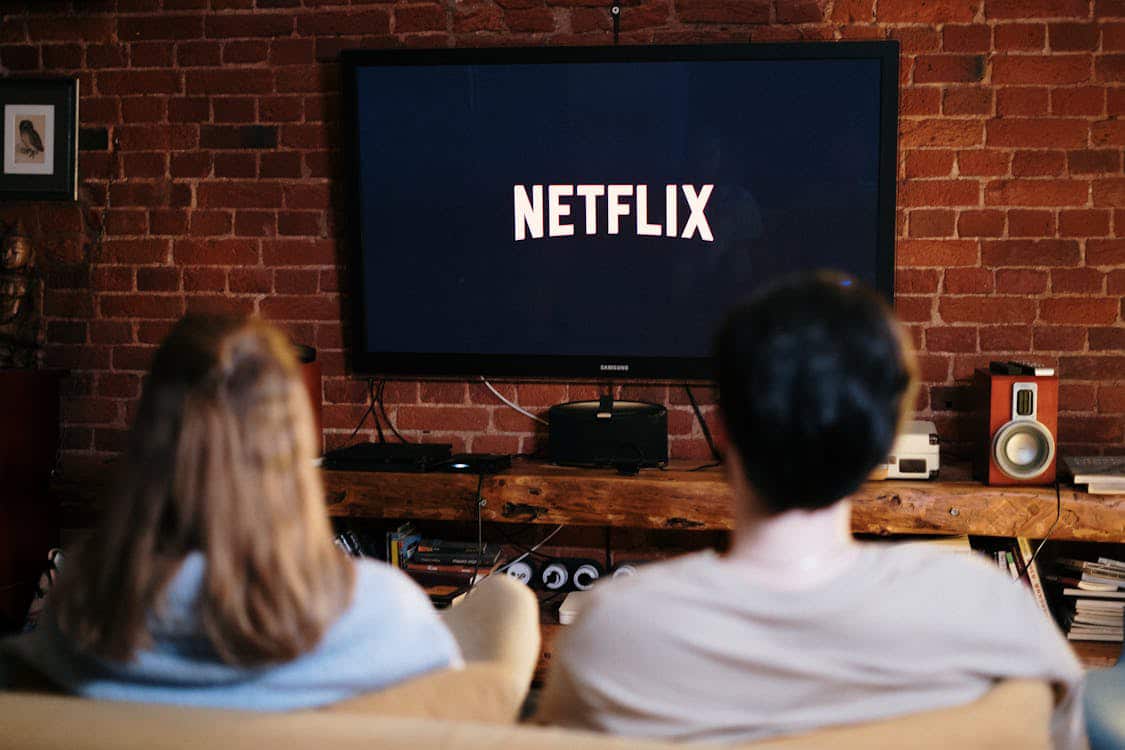 A couple relaxes on a couch, watching Netflix on a TV.