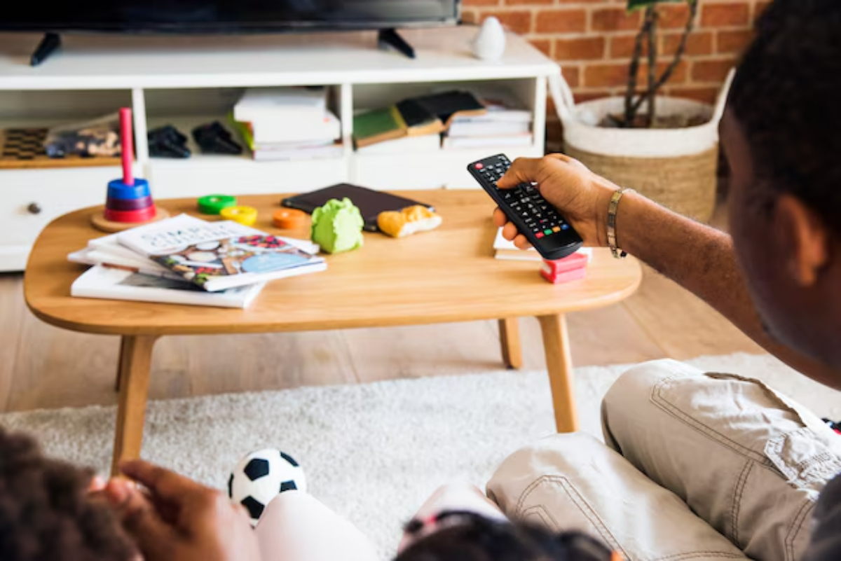 A person controls a TV remote while sitting on a sofa.