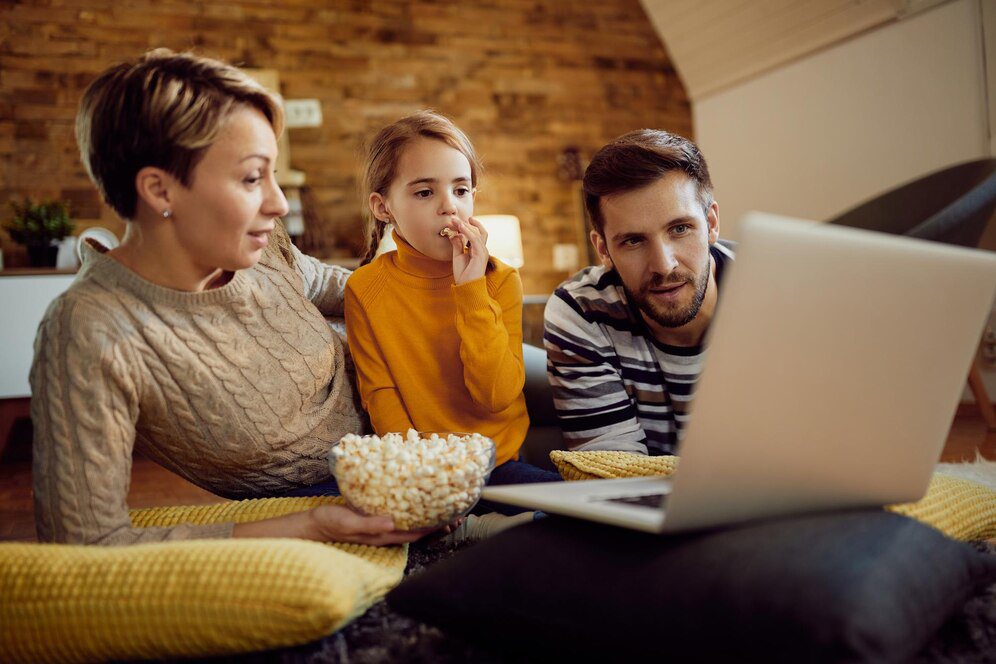 A family enjoys popcorn while watching a movie on a laptop.