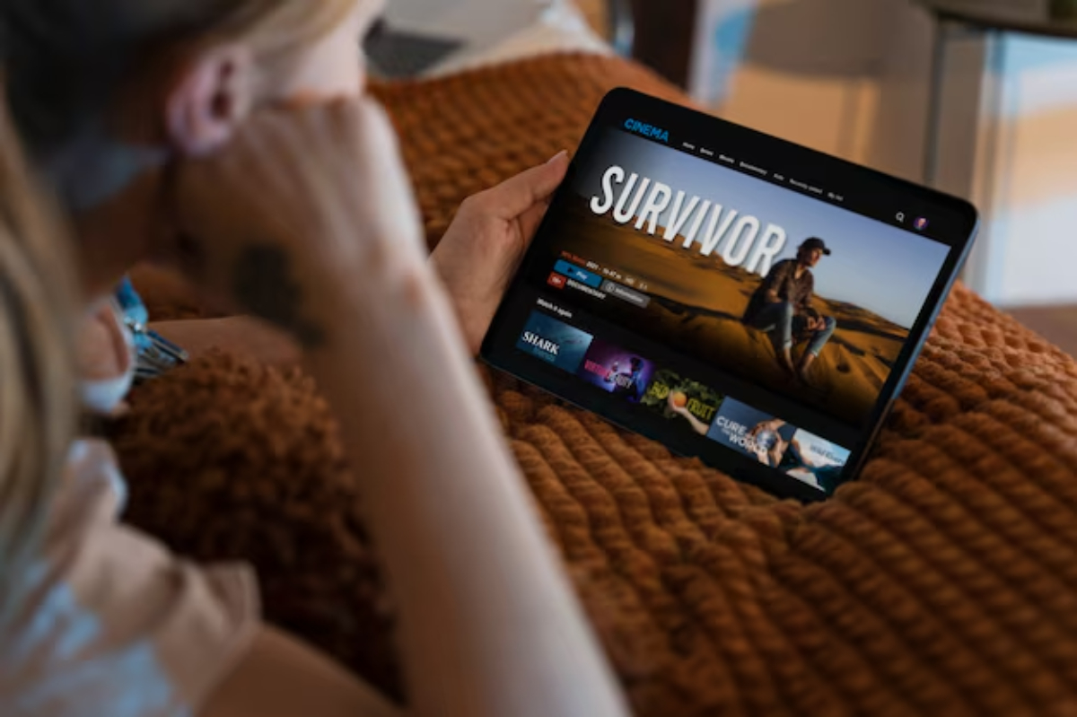 A person sits on a couch, intently watching a tablet.