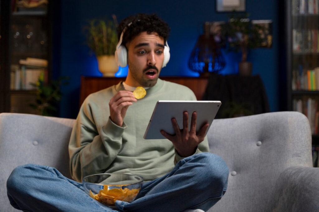 A person wearing headphones enjoys snacks while using a tablet.