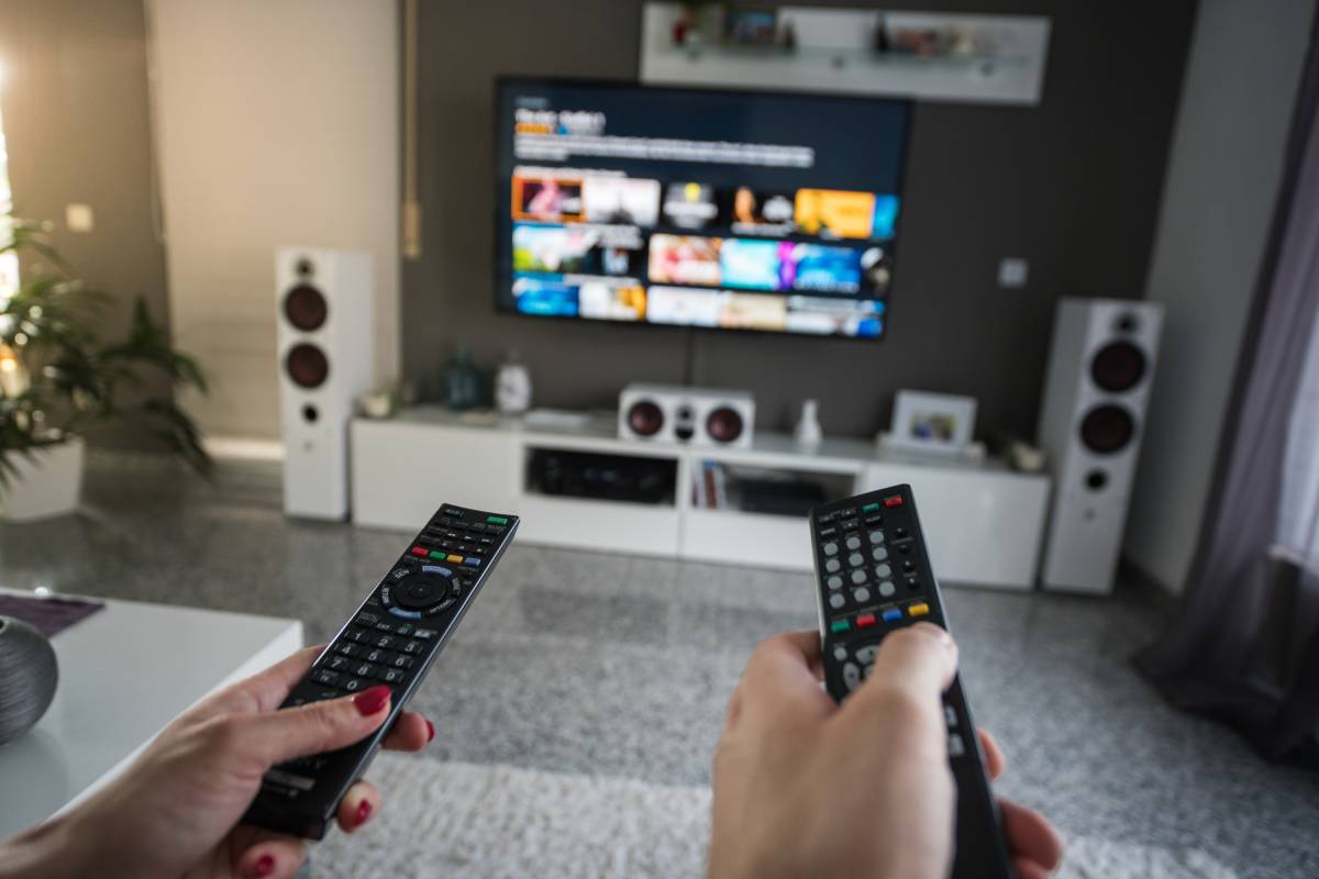 A living room setting featuring two hands holding remote controls.
