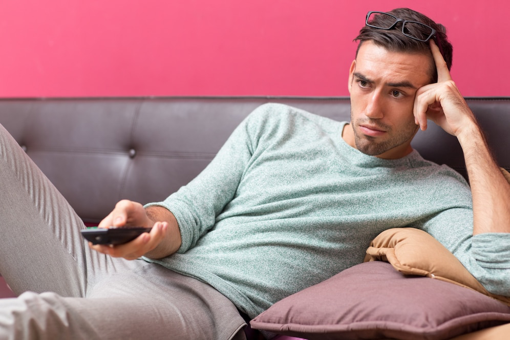 A person lounging on a couch, wearing a green sweater, holding a remote.