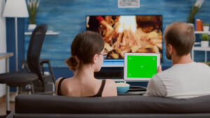 A couple sits on a couch, watching a TV displaying a fire scene.