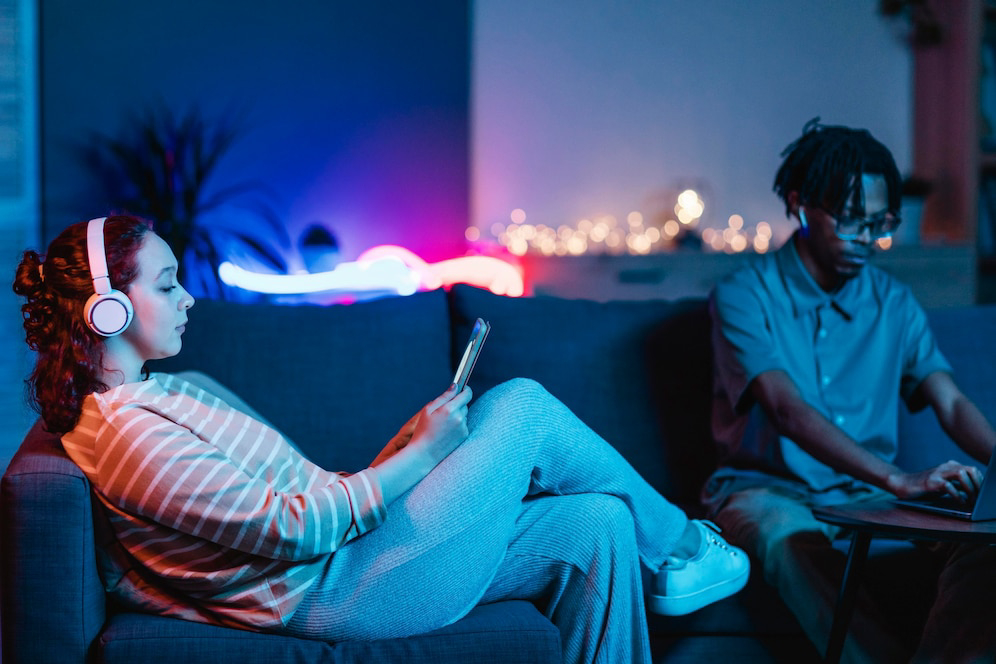 A woman in headphones relaxes on a couch, looking at her phone.