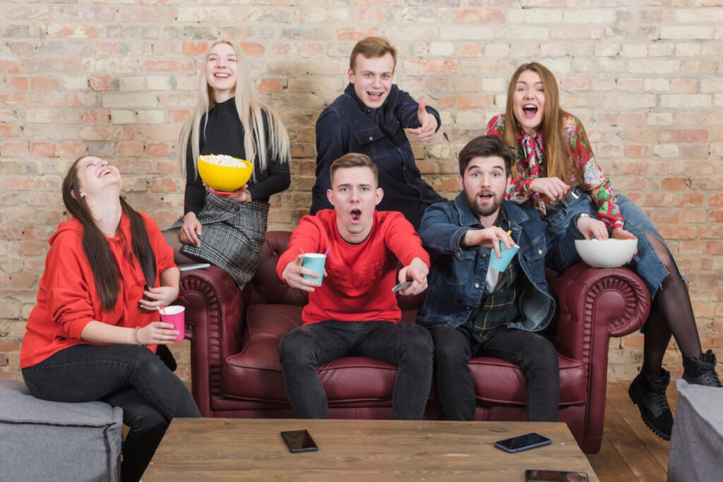 A group of six people enjoying snacks and drinks on a leather couch.