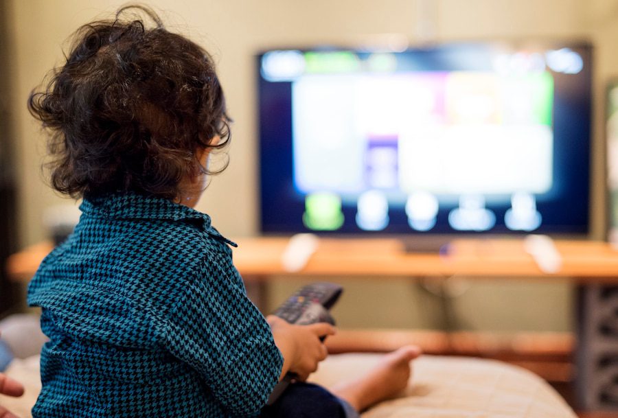 A young child sits on a sofa while holding a remote.