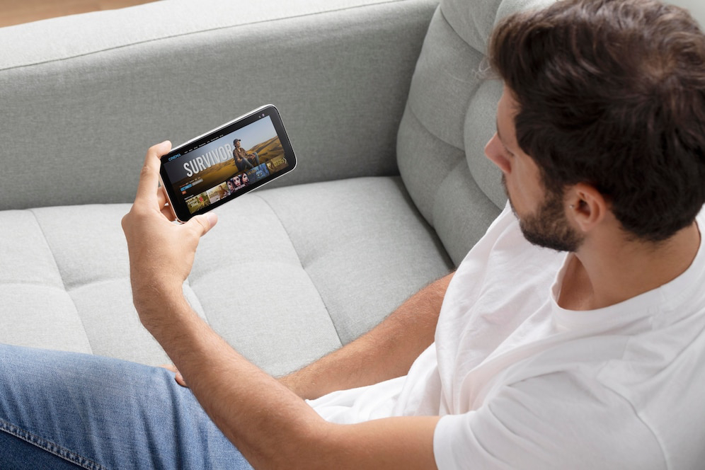 A person sits on a gray couch, holding a smartphone.