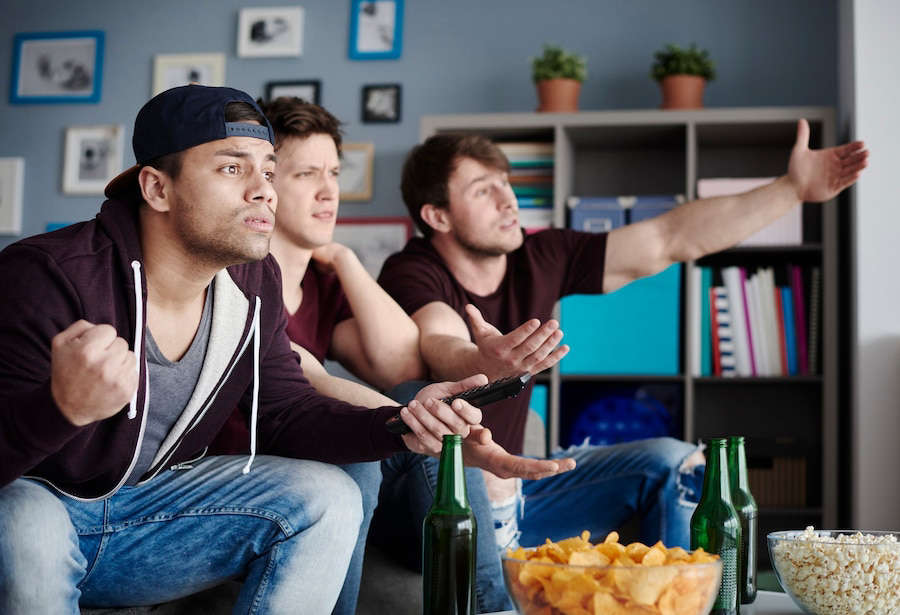 A group of friends sitting on a couch, engaging excitedly while watching TV.