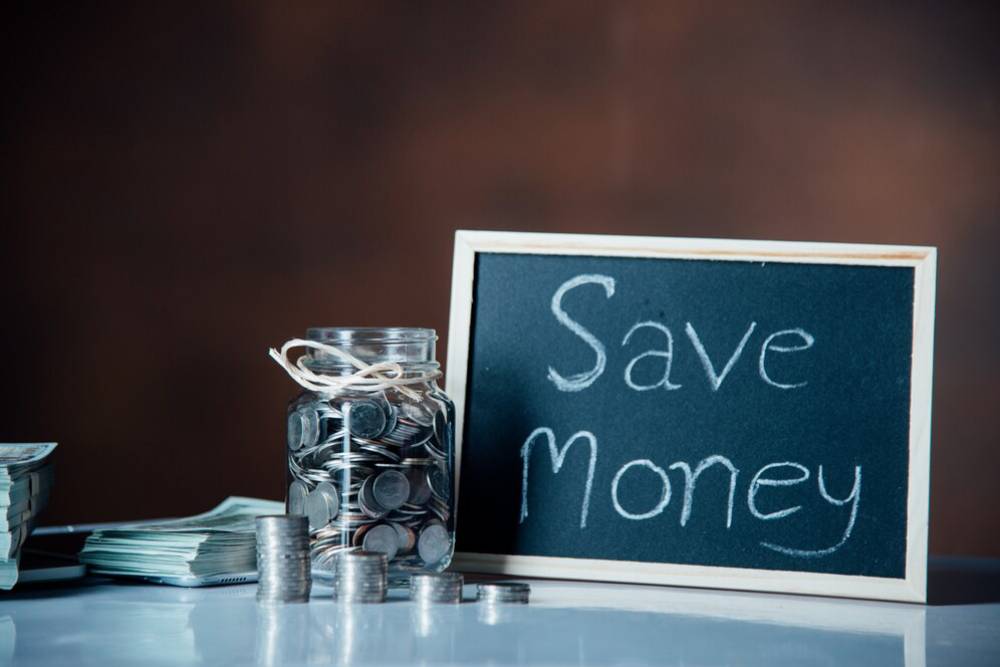 A jar filled with coins, stacks of banknotes, and a chalkboard displaying 