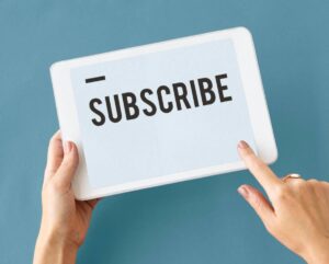Hands holding a digital tablet with the word "SUBSCRIBE" on the screen against a blue background.