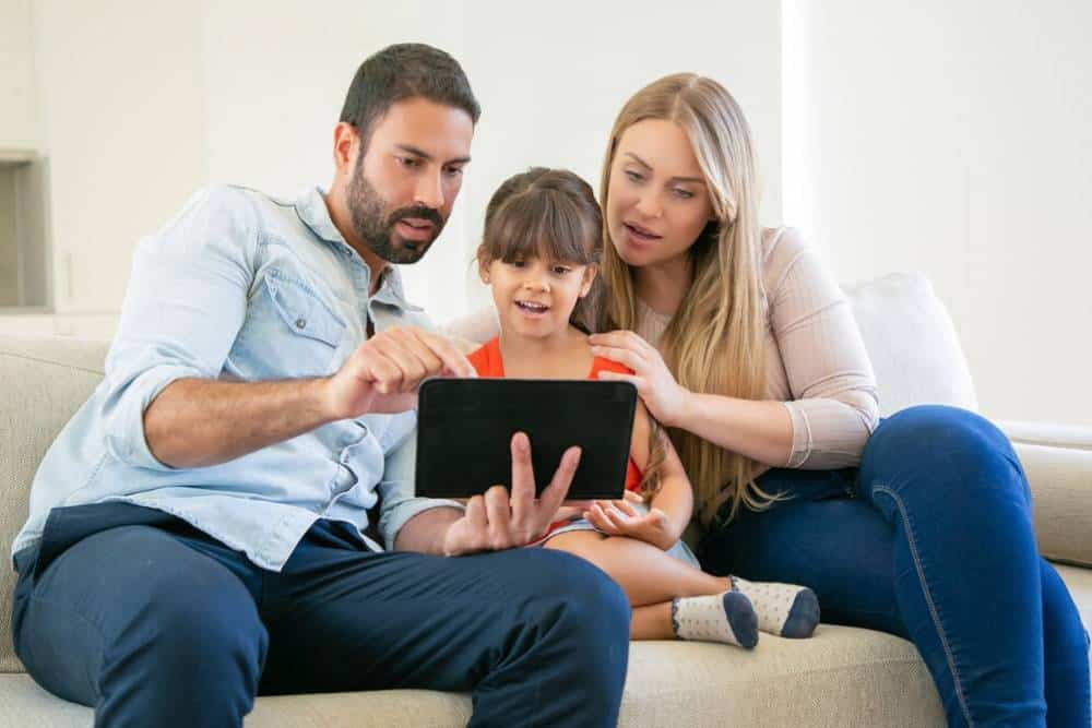 A family with a young girl using a tablet together on a sofa.