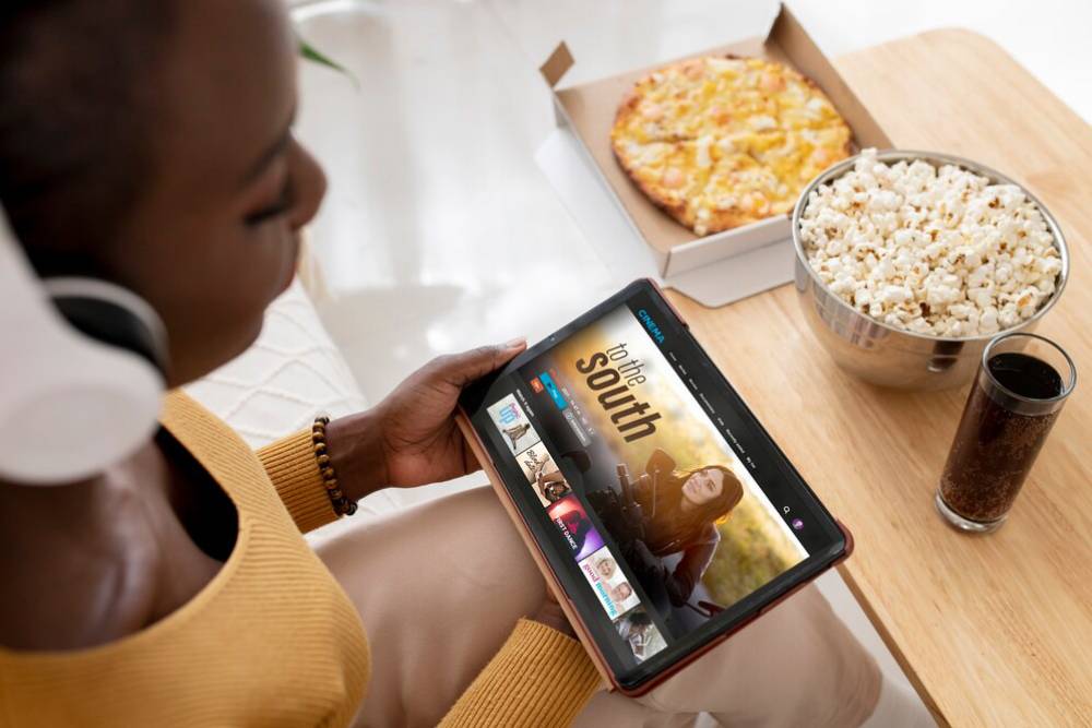 A person using a tablet to browse a streaming service, with pizza and popcorn nearby.