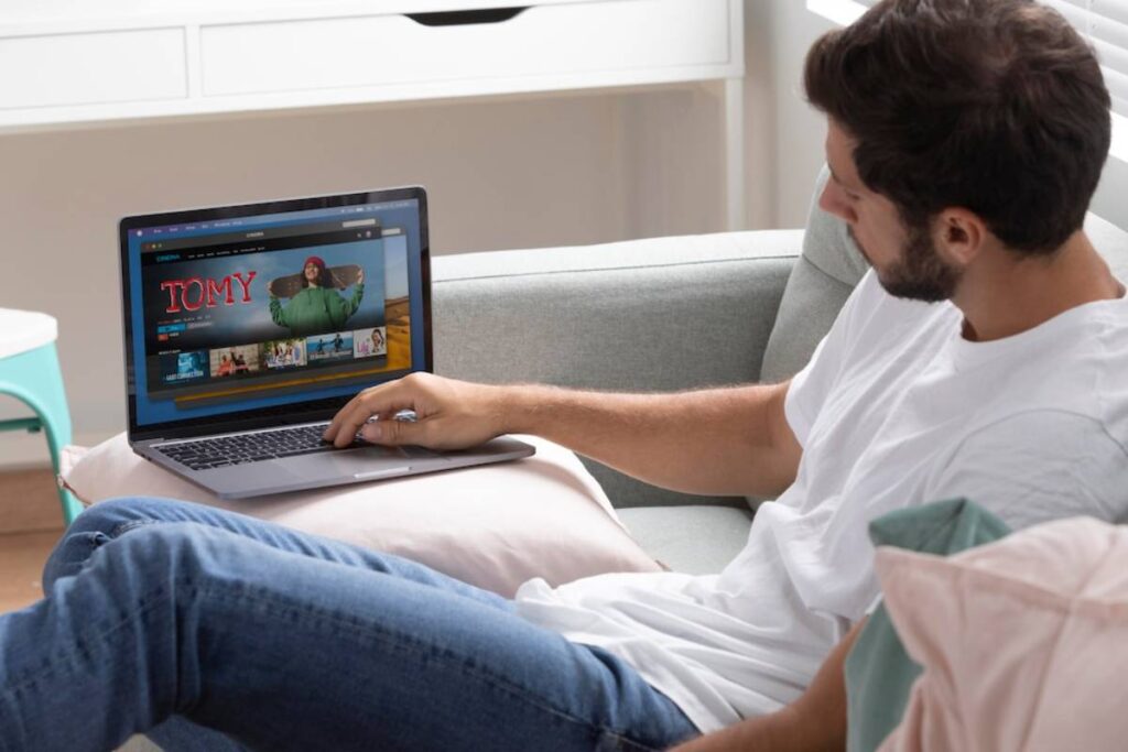 Man lounging on a sofa, using a laptop with a streaming service on screen.
