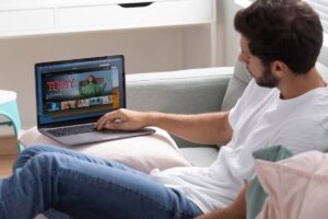 Man lounging on a sofa, using a laptop with a streaming service on screen.
