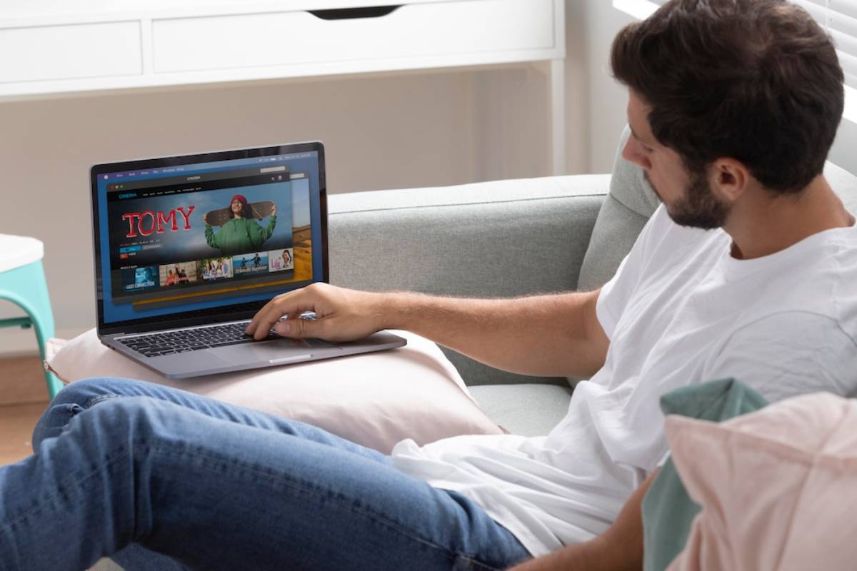 Man lounging on a sofa, using a laptop with a streaming service on screen.