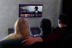 Three people sitting on a couch watching a movie titled "The Inspector" on a modern TV screen in a cozy living room.