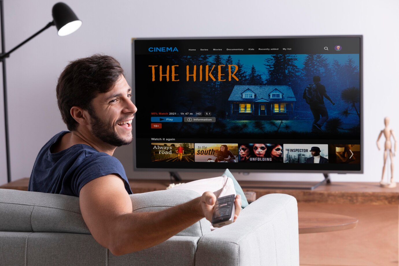 A person sits on a couch, holding a remote, watching a  movie on a large TV screen.
